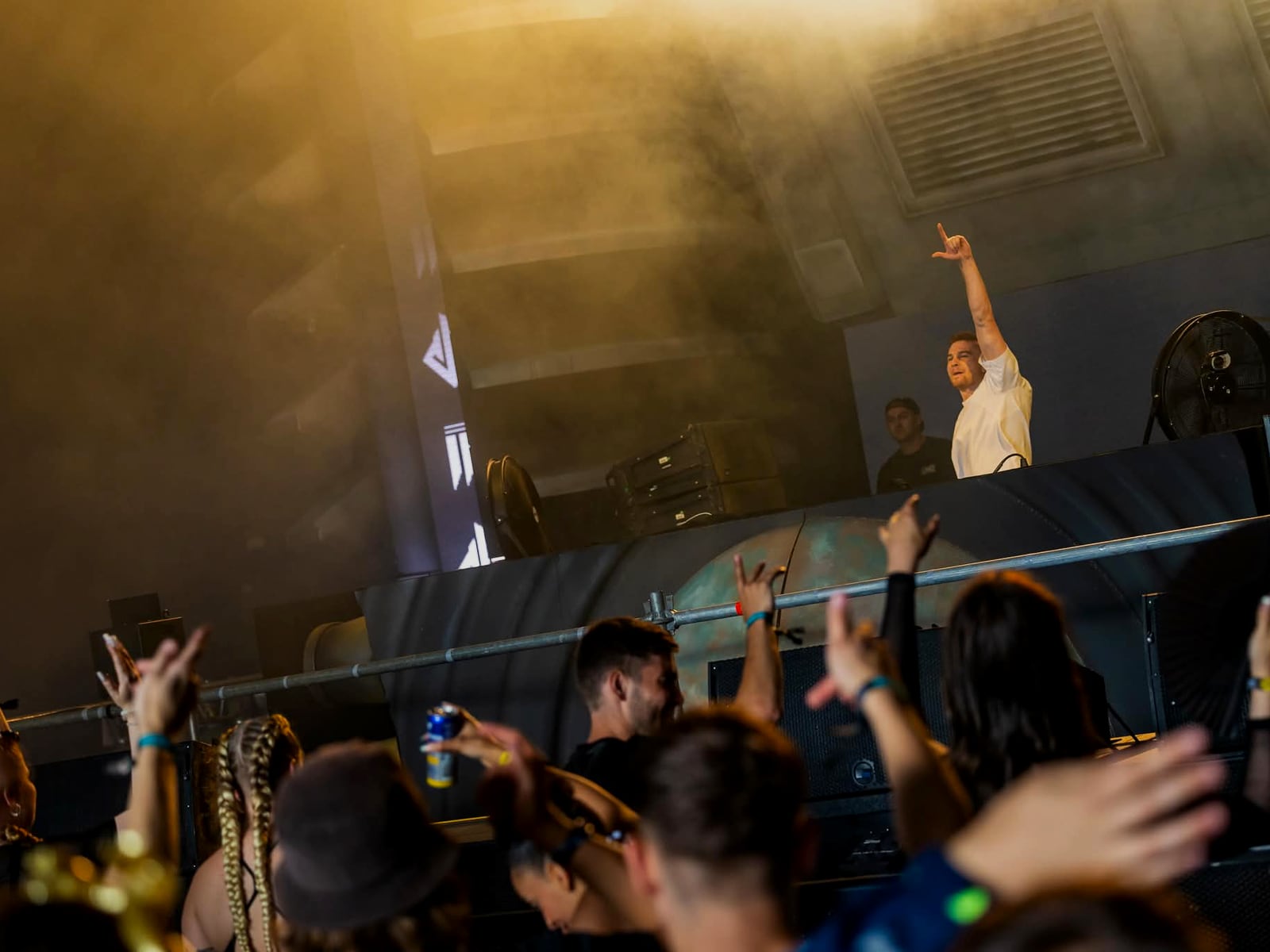 The crowd from behind, arms up, warm gold light over the stage