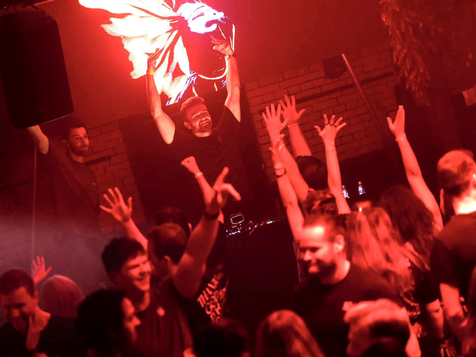 A packed floor with hands in the air under deep red light